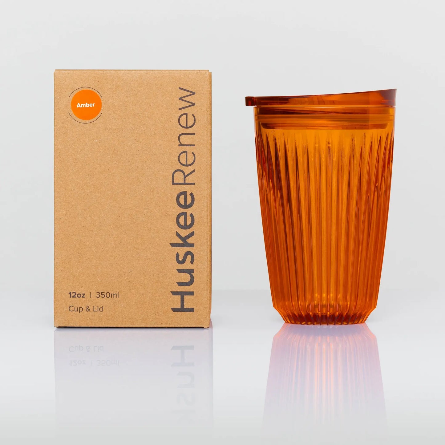 12 oz HuskeeRenew cup on white background. The cup is amber in colour and clear. There are vertical ridges running around the entire circumferance. The carton is kraft brown with huskee branding printed on the side.